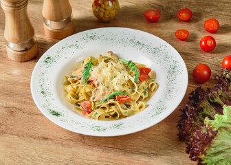 Noodles with cheese and tomatoes in a white sauce with herbs and cherry tomatoes on a white plate on a wooden table.