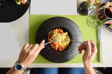 Noodles with tomato sauce, cheese, basil and chili on a black plate, top view. A beautiful restaurant dish. Table setting.