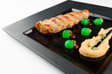 Meat with sauce and garnish on a black square plate. A beautiful restaurant dish.