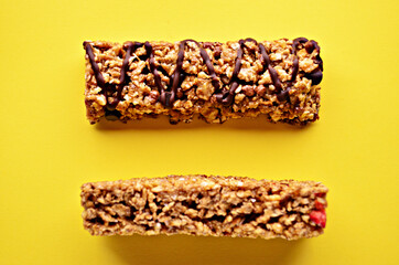 Bars of granola with chocolate and cranberries lie on the table of yellow color close-up view from above. High quality photo