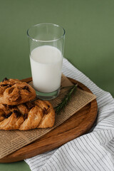 Useful breakfast on a wooden tray. Glass of milk and pastries with raisins on a green background.