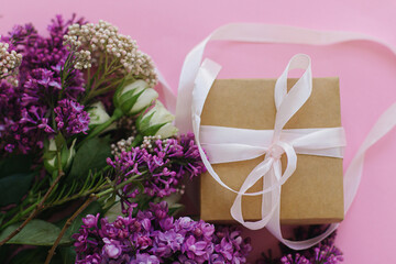 Simple gift box and lilac and roses bouquet flat lay on bright pink background. Happy mothers day