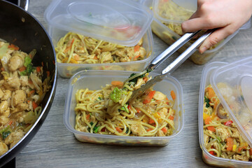Chicken Noodles Being Transferred To Plastic Food Containers Using A Pair Of Kitchen Tongs