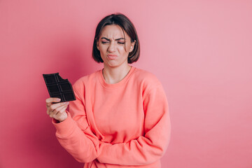 Beautiful sad woman with abdominal pain with chocolate bar on pink background and bright makeup