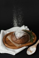 Flour is sprinkled on freshly baked bread on a black background. Round bread on a wooden tray. Natural food.