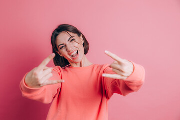 Woman wearing casual sweater over pink background shouting with crazy expression doing rock symbol...
