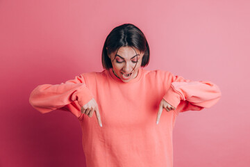 Woman wearing casual sweater on background pointing down with fingers showing advertisement, surprised face and open mouth