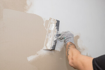 hand of builder worker plastering at wall.Renovation workers hand plastering the wall.Construction finishing works.work aligns with a spatula wall.process of applying layer of putty trowel