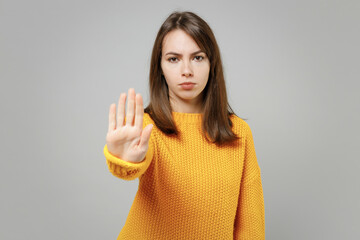 Young serious strict caucasian attractive woman 20s in casual knitted yellow sweater doing stop...