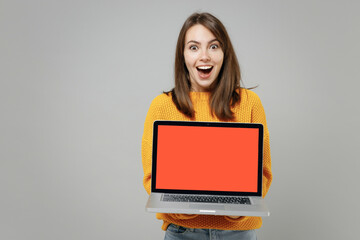Naklejka premium Young smiling freelancer copywriter attractive caucasian woman 20s in knitted yellow sweater hold laptop pc computer with blank screen workspace area isolated on grey color background studio portrait