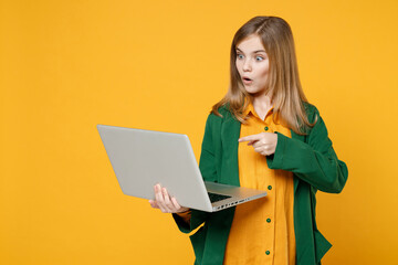 Little blonde pretty cute kid girl 12-13 years old wearing casual clothes point index figer on laptop pc computer isolated on yellow background children studio portrait. Childhood lifestyle concept