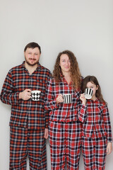 Family in pajamas on a white background. Dad, mom and little daughter with cups of tea. They smile, fool around, build funny faces and looking at camera. father's, mother's and baby's day.