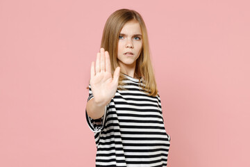 Little blonde serious strict kid nice girl 12-13 years old in striped oversized t-shirt show palm gesture refusing look camera isolated on pastel pink background children. Childhood lifestyle concept.