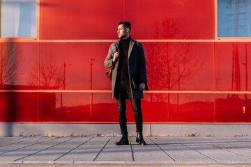 Young businessman with backpack and laptop in front of a red wall at sunset
