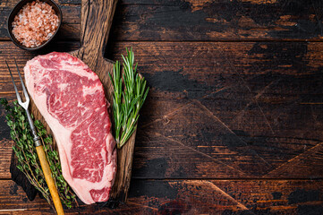 Raw new york strip beef steak or striploin on a wooden board. Dark wooden background. Top view....