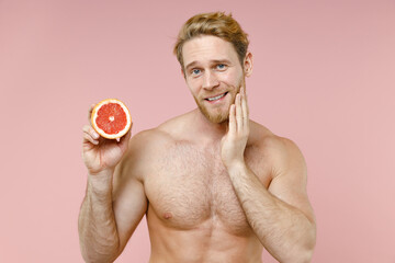 Smiling bearded naked young man 20s years old perfect skin hold half fresh grapefruit put hand on...