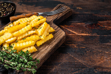 Baked Crinkle French fries potatoes sticks or chips  on a wooden board. Dark wooden background. Top view. Copy space