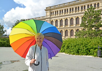 A mature woman under a rainbow umbrella stands against the background of the exchange building. Kaliningrad