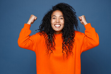 Happy joyful young african american woman in casual basic orange sweatshirt doing winner gesture...