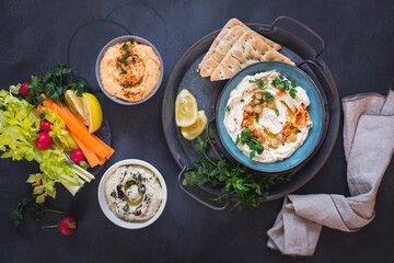 Various types of hummus served with fresh vegetables and pita bread. Top view, blank space