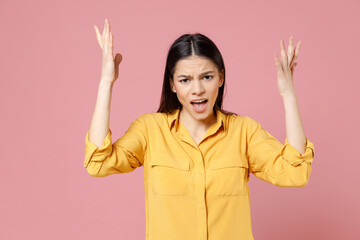 Young brunette angry indignant confused latin wondered woman 20s wearing yellow casual shirt spreading hands screaming shouting looking camera isolated on pastel pink color background studio portrait.