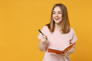 Young dreamful happy smiling student woman 20s wearing casual basic pastel pink t-shirt writing...