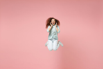 Full length young black african fun happy surprised shocked excited woman 20s wearing blue shirt scream news with hands near mouth jump high isolated on pastel pink color background studio portrait.