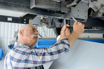senior mechanic checking underneath vehicle