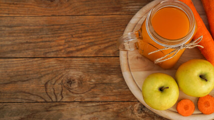 Apple and carrot juice in glass, fresh vegetables and fruits on wooden background. Rustic style. Homemade drink with vitamins