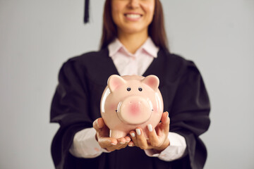 Education fund. Close up of a piggy bank in the hands of a female student on a gray background. Concept of finance, tuition and saving money. Blurred background.
