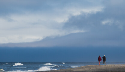 A man and woman holding hands and walking on the beach at Neskown on the Oregon coast.