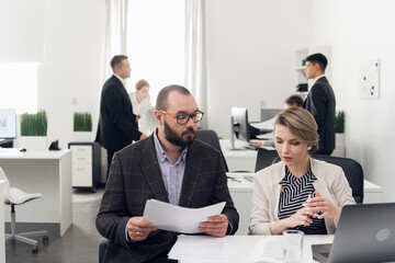 The senior Manager checks the quality of tasks performed by his Junior employees sitting at a computer in the office of a financial company.