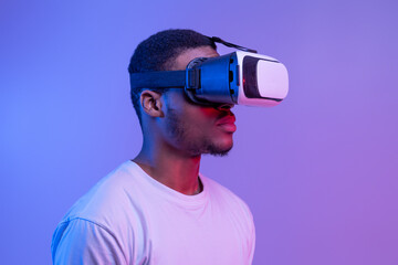 Black Man In VR Headset Standing In Neon Light Over Purple Background