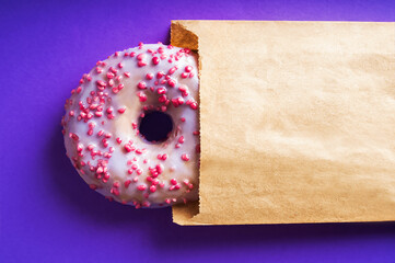 Donut with purple and pink powder close-up on blue background. Food delivery concept, donut in kraft wrapping paper and copy space.
