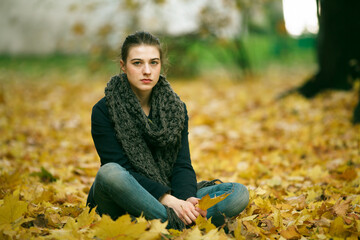 Girl sitting on fallen leaves in the autumn park.