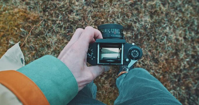 Hand of a man holding a vintage camera and looking through the visor a natural scenery.
