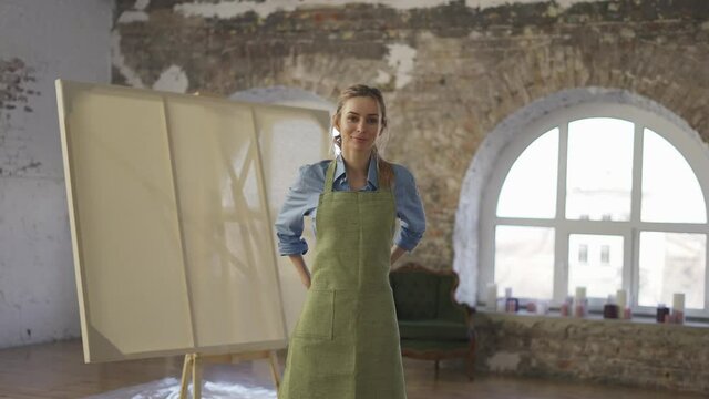 Portrait smiling woman wearing apron to start painting in workshop