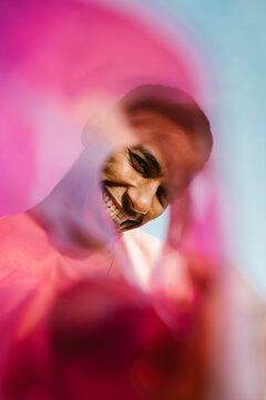 Smiling man looking through rolled up plastic against sky