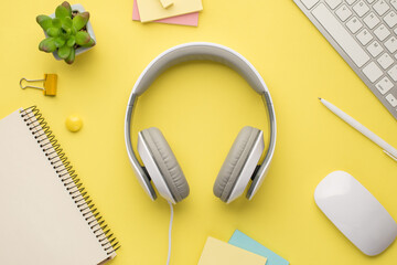 Photo above of headphones plant keyboard notebook pen notes paperclips and computer mouse isolated on the yellow background