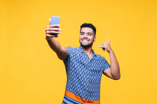 Smiling man gesturing while taking selfie through mobile phone against yellow background