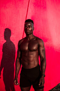 Male athlete looking away while standing by red wall during sunset