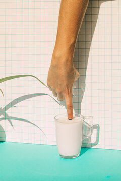 Female putting finger in milk cup on blue table