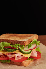 Appetizing sandwich serving on parchment paper on black background with copy space.