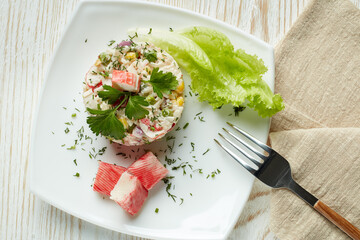 Appetizing salad from crab sticks with rice and vegetables on light wooden table. Top view