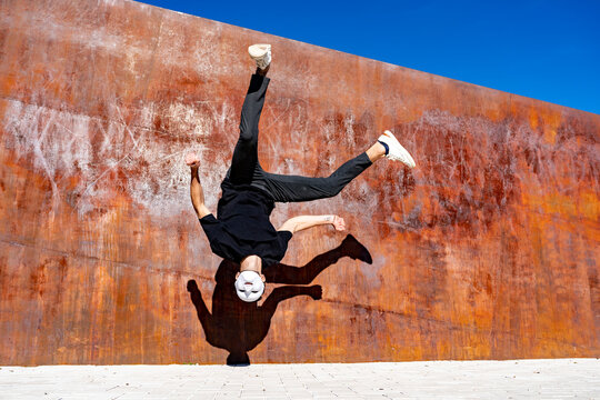 Man Wearing Whit Mask Jumping Against Brown Wall During Sunny Day