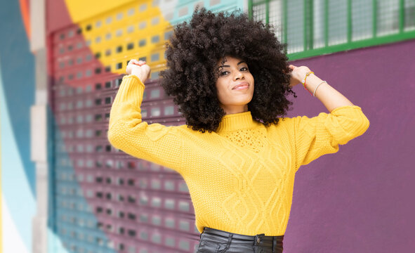 Curly hair woman smiling while standing against multi colored wall