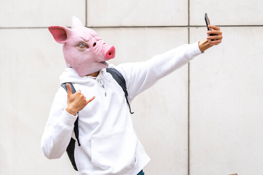Man with pig mask taking selfie on smart phone against wall