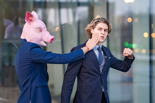 Businessman slapping male coworker while him showing fist by glass wall