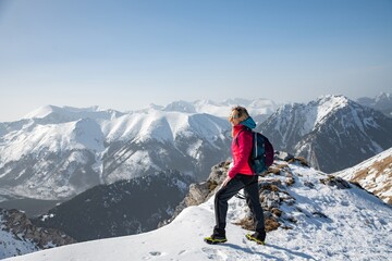 A blonde tourist is standing on the top of the mountain. He admires the beautiful winter landscape. Mountain tourism.