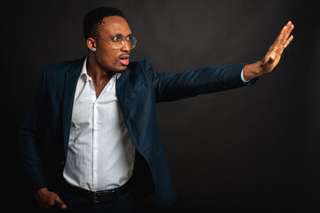 Portrait of an attractive, handsome, stylish professional African American businessman in a stylish suit and white shirt, isolated on a dark background, hands shows that everything will be ok. Low key